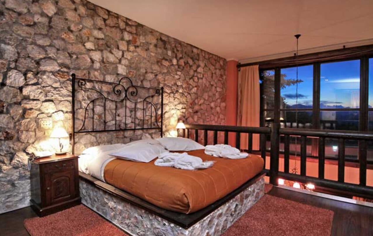 Υπνοδωμάτιο της Grand Suite με πετρόκτιστο τοίχο και πόρτα στο μπαλκόνι